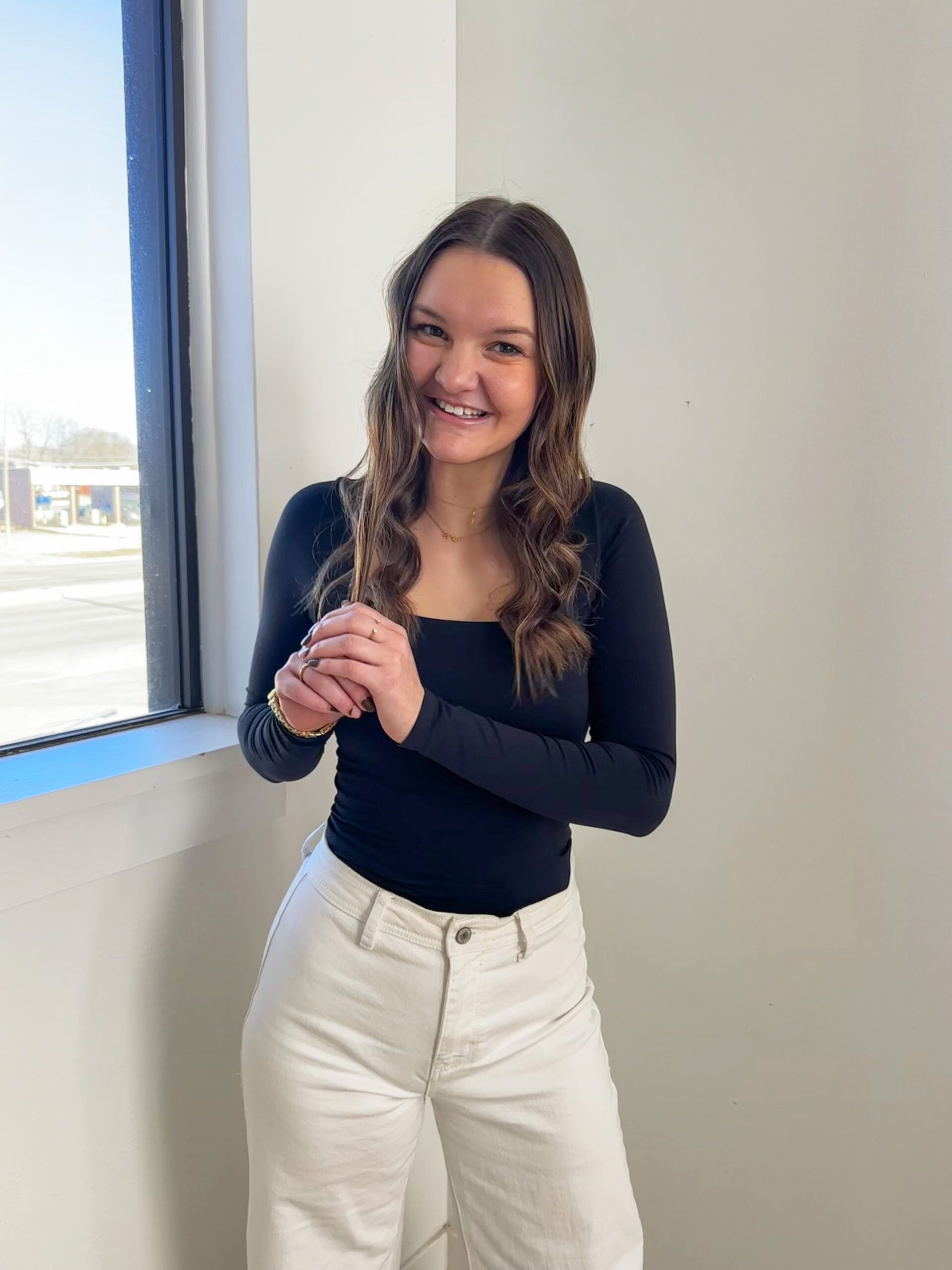 profilepic Travianna Tighe in a black long sleeve and white jeans in front of a white wall.