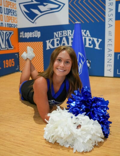 Cheerleader Addie Buhlke poses on the ground with her poms for a media day photo.