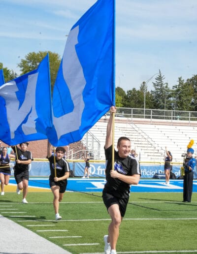 Josiah Gonzales and the cheer carry UNK flags to lead the Football team out of the Locker Room.